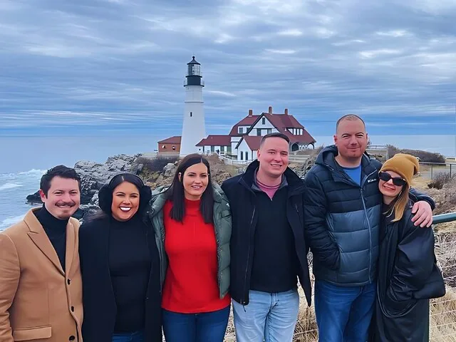 Gruppo di sei persone che sorridono insieme davanti al Portland Head Light