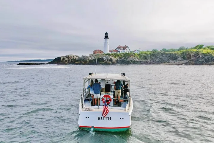 Una piccola barca da tour di nome 'RUTH' si dirige verso il Portland Head Light in una giornata nuvolosa